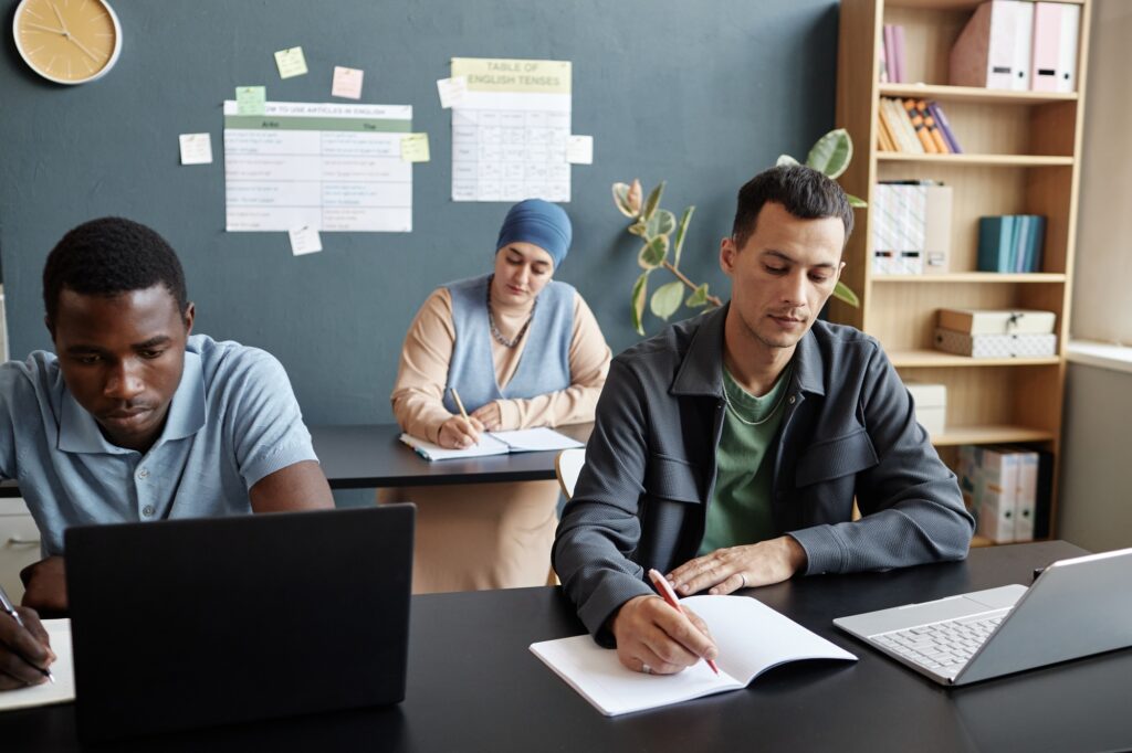 Adult Man Writing Test in Exercise Book at Desk while Studying English in Group Class