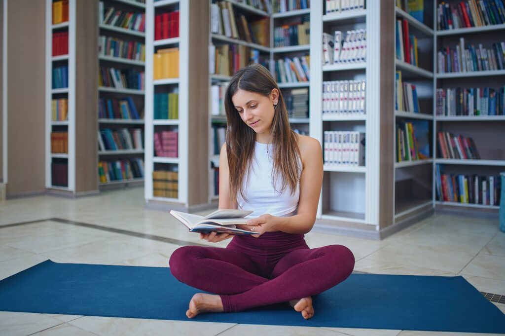 Beautiful young woman reading book and practices yoga
