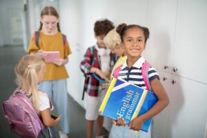 Dark-skinned girl with English grammar book standing near friends