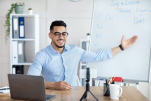 E learning. Arab male teacher giving online English lesson on smartphone, pointing at blackboard