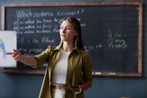 Female Teacher with Table Speaking to Student in English Class at Language School