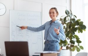 Joyful young teacher standing near blackboard, explaining grammar, giving online lesson to students