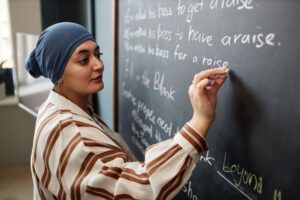 Muslim Woman Writing Sentences on Chalkboard Studying English in Classroom