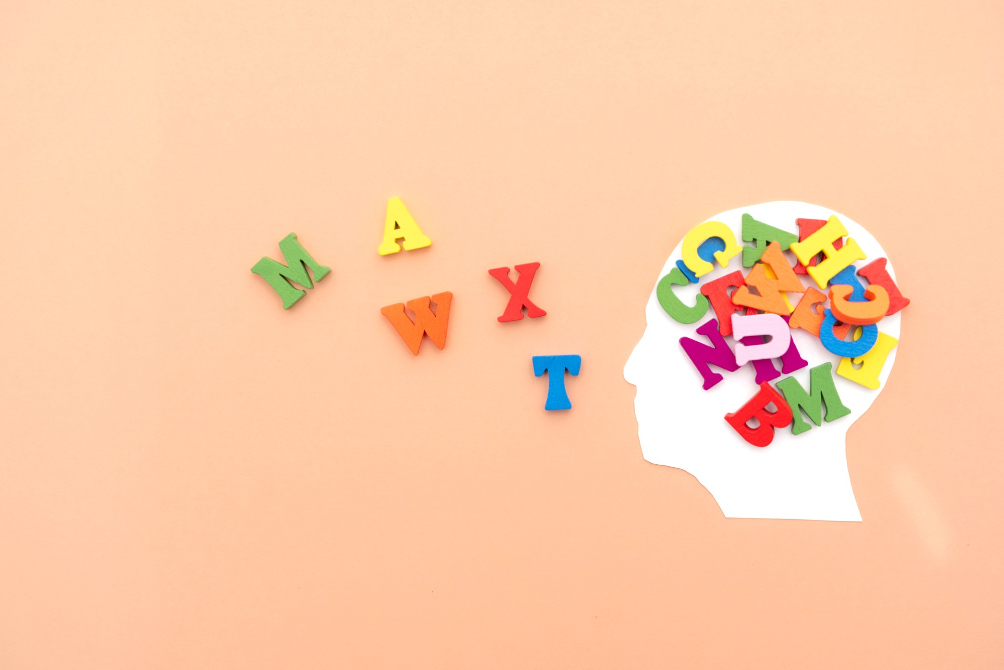 Silhouette of a human head Overflowing with colorful letters on peach background,