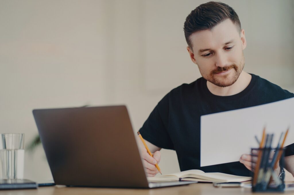 Skilled professional male expert busy doing paper report edits online files via laptop