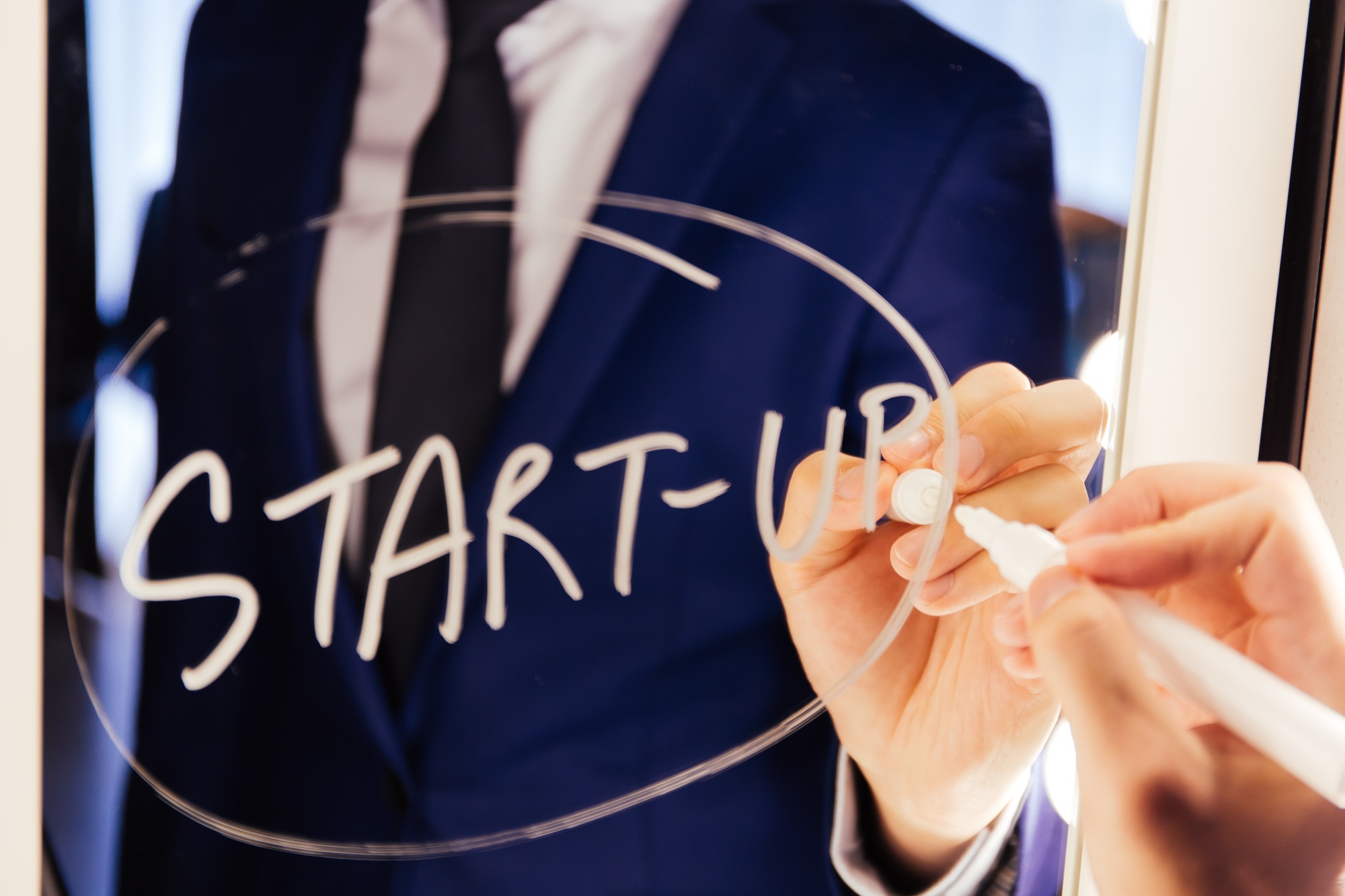 Smart business man writing the word Start-up on the mirror board