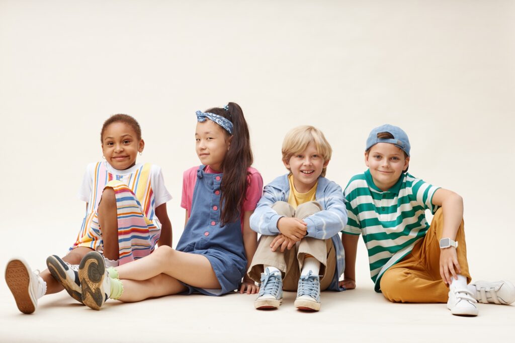 Smiling Kids in Colorful Clothes Sitting on Studio Floor against Neutral Background