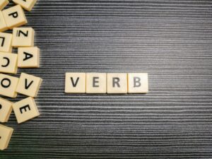 Word verb made from square letter tiles against black background.