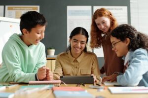 Young cheerful teacher and group of pupils looking at tablet screen