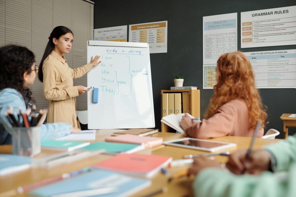Young confident teacher standing by whiteboard with English grammar rules