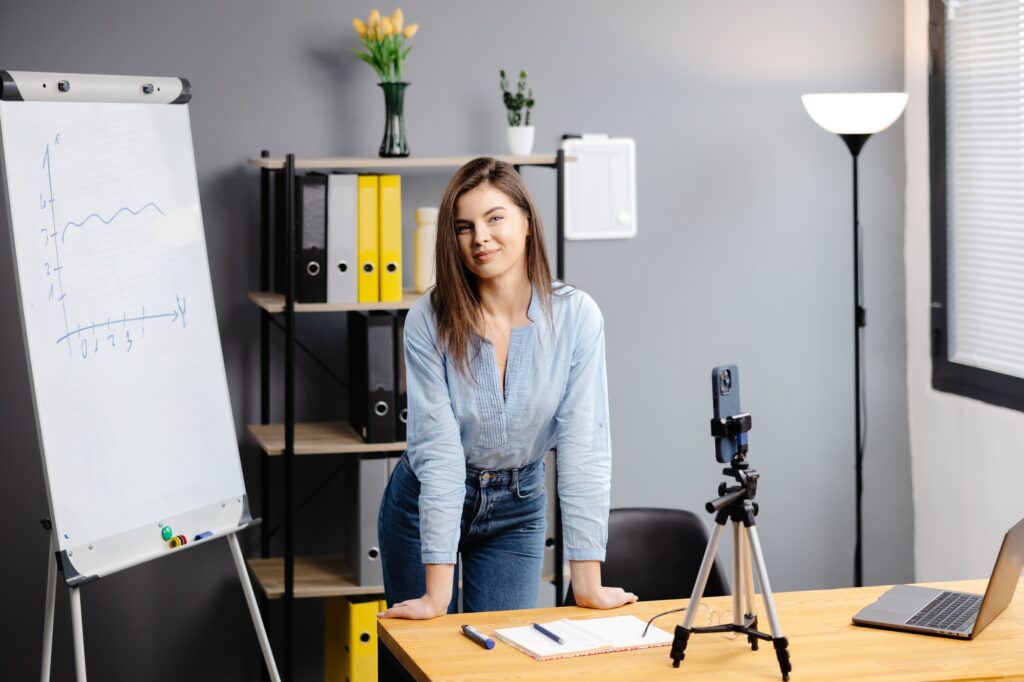 Young woman mentor recording presentation, webinar on smartphone standing on tripod